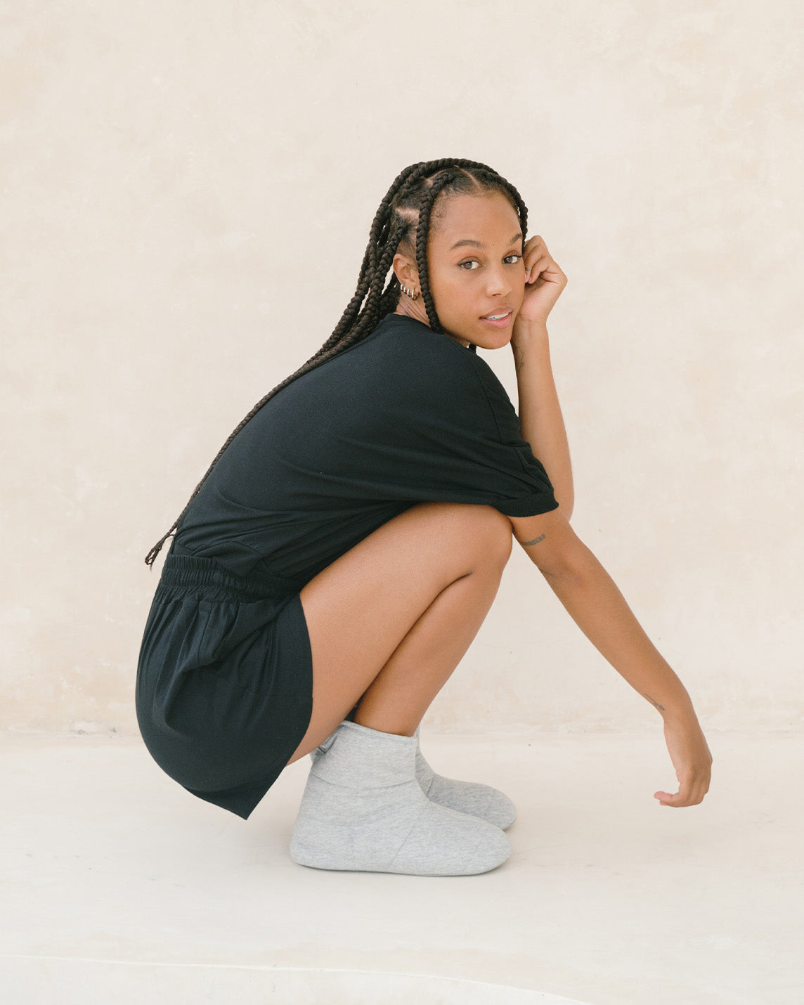 A woman bends down wearing grey cotton slippers [43579501084891, 43579501117659, 43579501150427, 43579501183195]